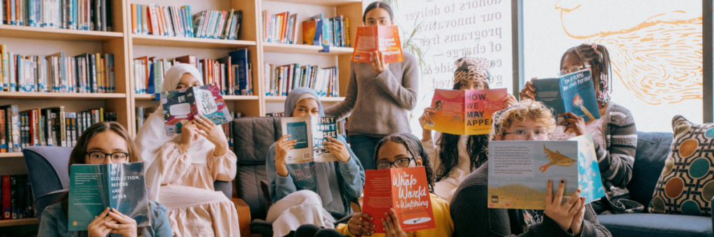 Eight 826 Boston Youth Literary Advisory Board members hold books up and pose. 