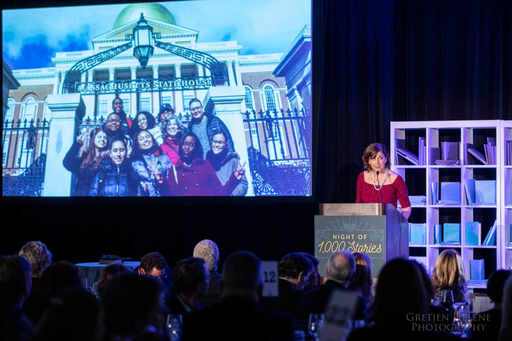 Jessica Drench speaking, a photo of students at the State House behind her.