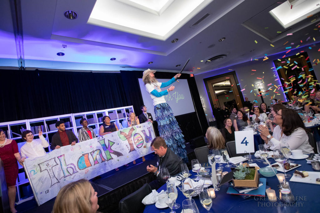 A stilt-walker firing a confetti cannon in front of a ‘Thank You’ banner.