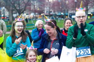 A group of people clapping, wearing unicorn horns and race bibs.