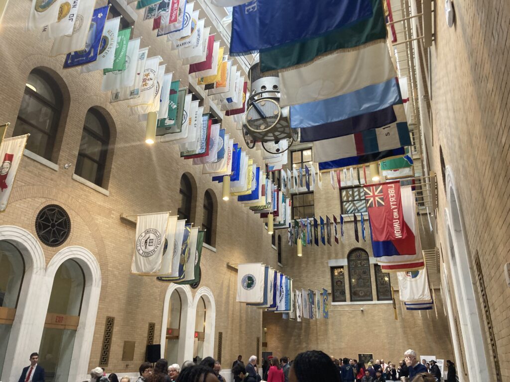 A photo taken during the Mass Cultural Council award ceremony. Several flags hang above a lobby that is filled with attendees.  