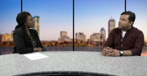 Boston Neighborhood Network’s News Director Faith Imafidon (left) and 826 Boston's Director of Programs and Community Engagement Jay Enciso (right) sit behind a news desk.